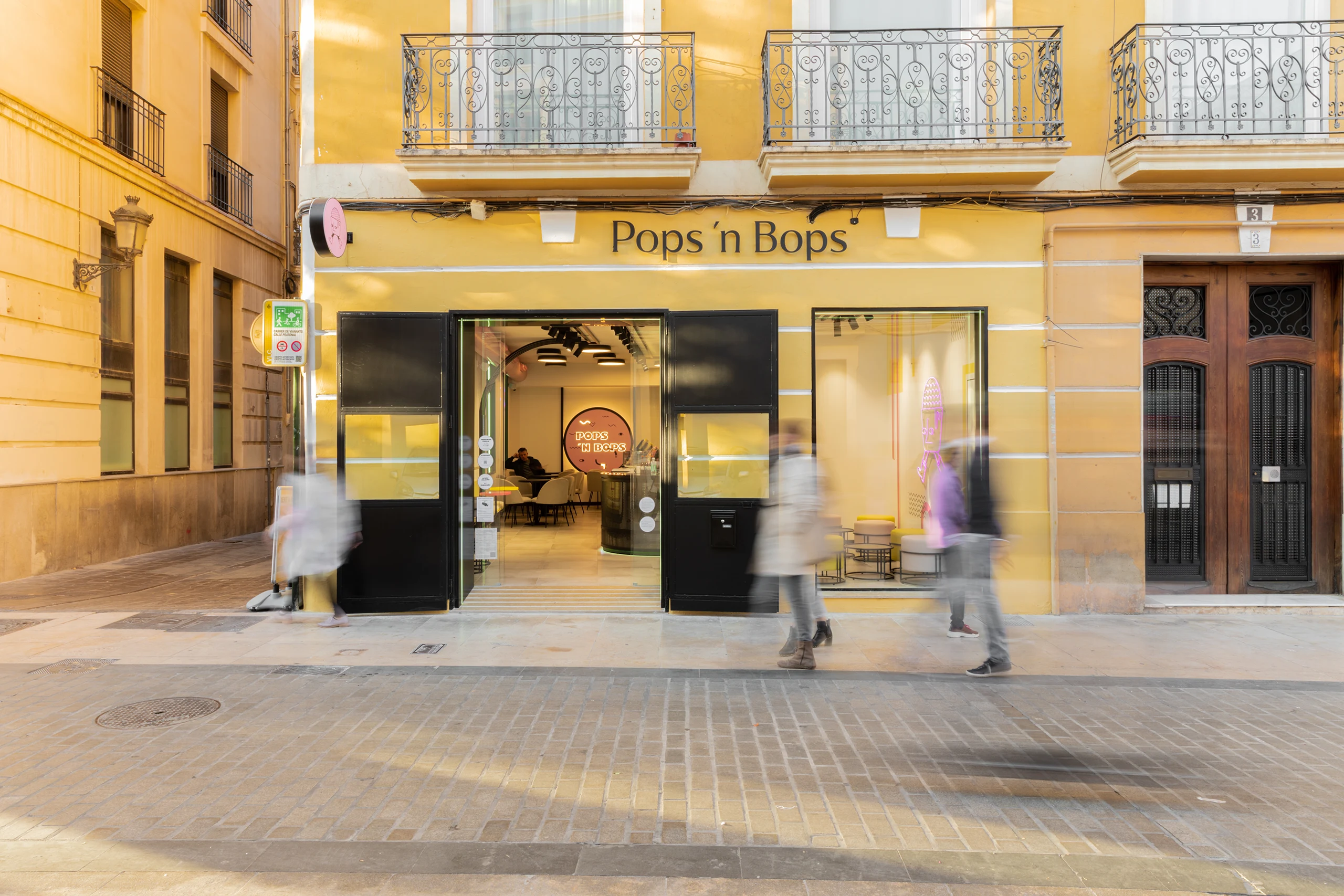 Fachada amarilla de heladería Pops 'n Bops en calle peatonal de Valencia con escaparate diseñado por huuun