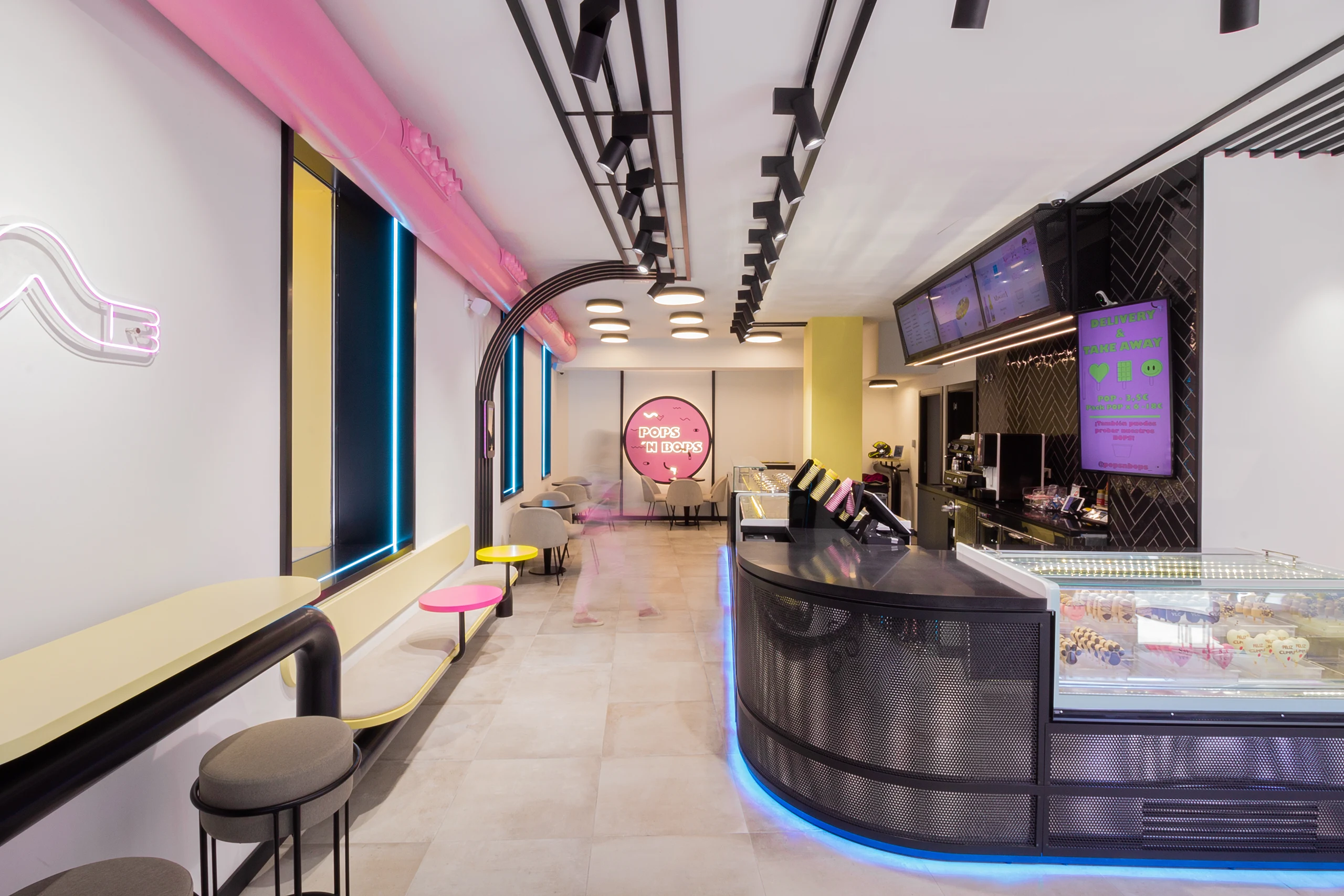 Interior de heladería Pops 'n Bops con barra negra, iluminación neón rosa y azul, y decoración pop diseñada por huuun