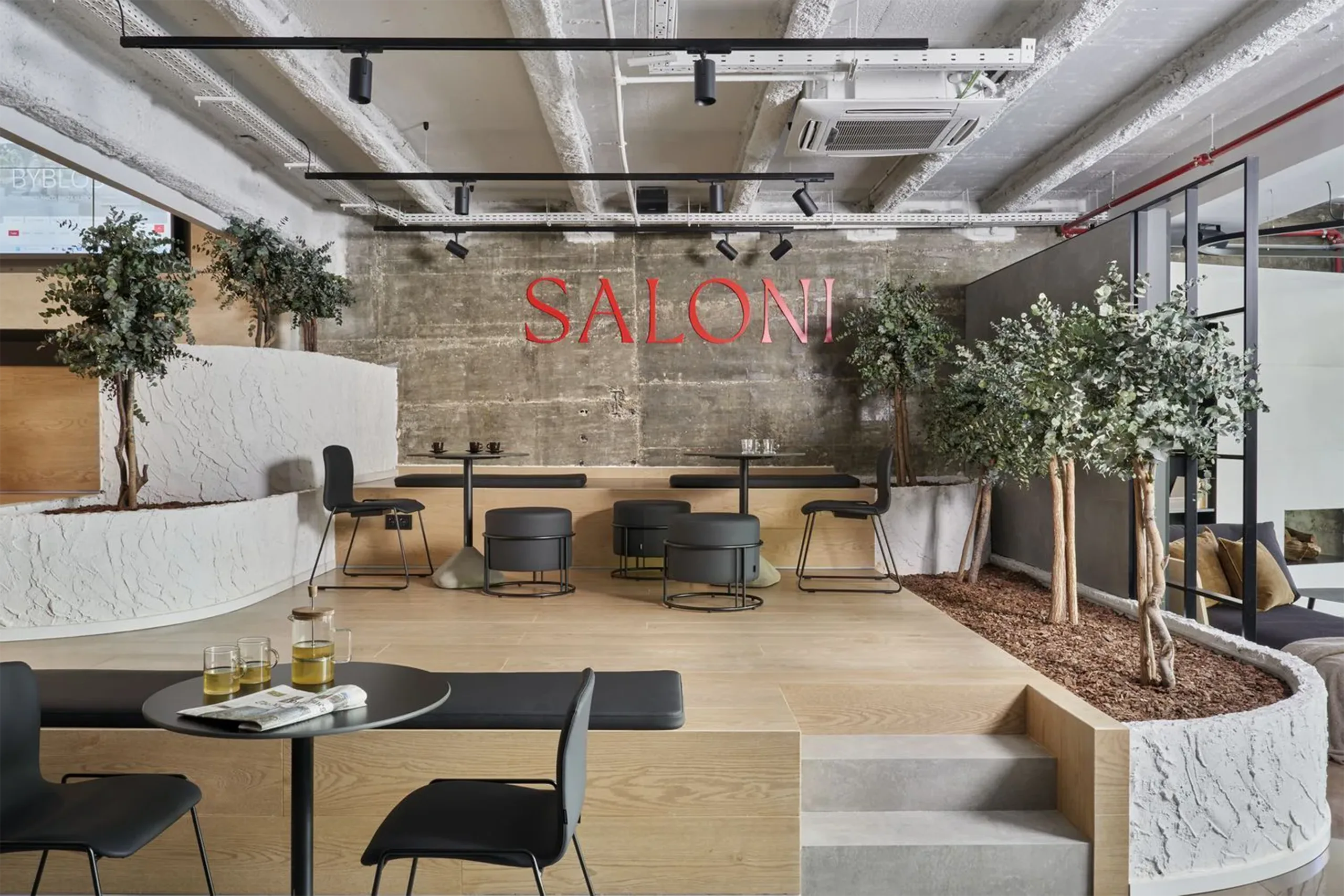 Zona de descanso del showroom SALONI Madrid con muro de hormigón visto, logo rojo, vegetación y mobiliario diseñado por huuun