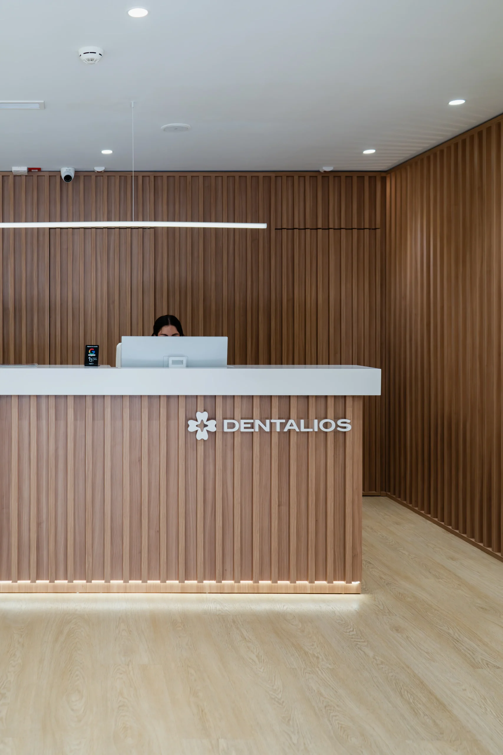 Mostrador de recepción de Dentalios revestido en listones de madera, con sobre en blanco, logotipo de la marca y pared de fondo también en madera