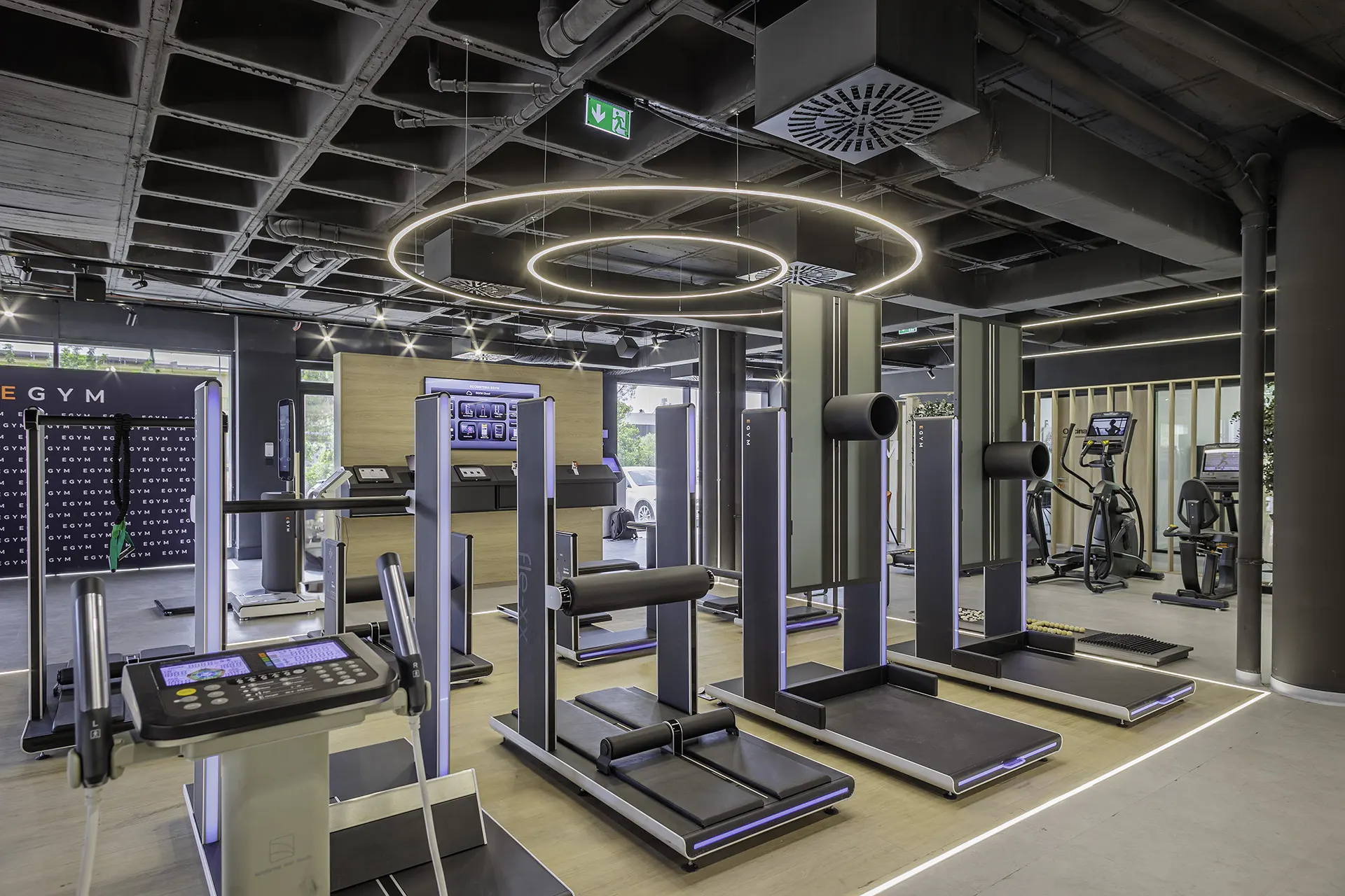 Espacio gym de EGYM Fitness Lab con máquinas EGYM de fuerza y cardio bajo techo técnico negro, anillos de luz LED circulares e iluminación RGB en violeta
