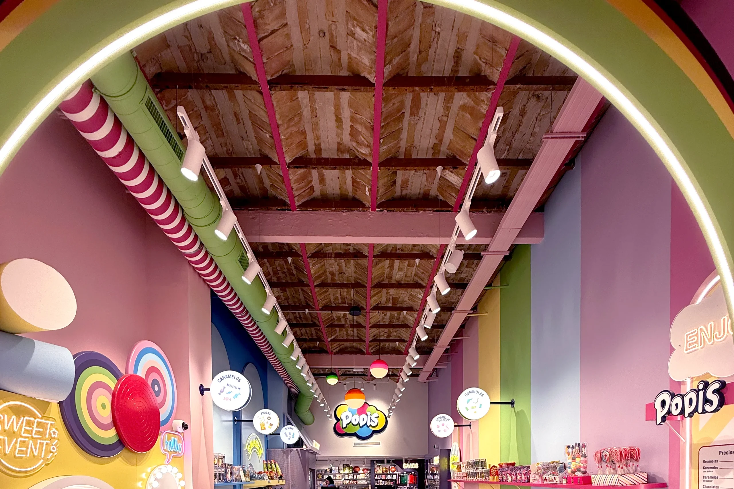 Techo original restaurado con vigas de madera y tubería decorativa a rayas sobre el pasillo principal de la tienda POPIS en Valencia