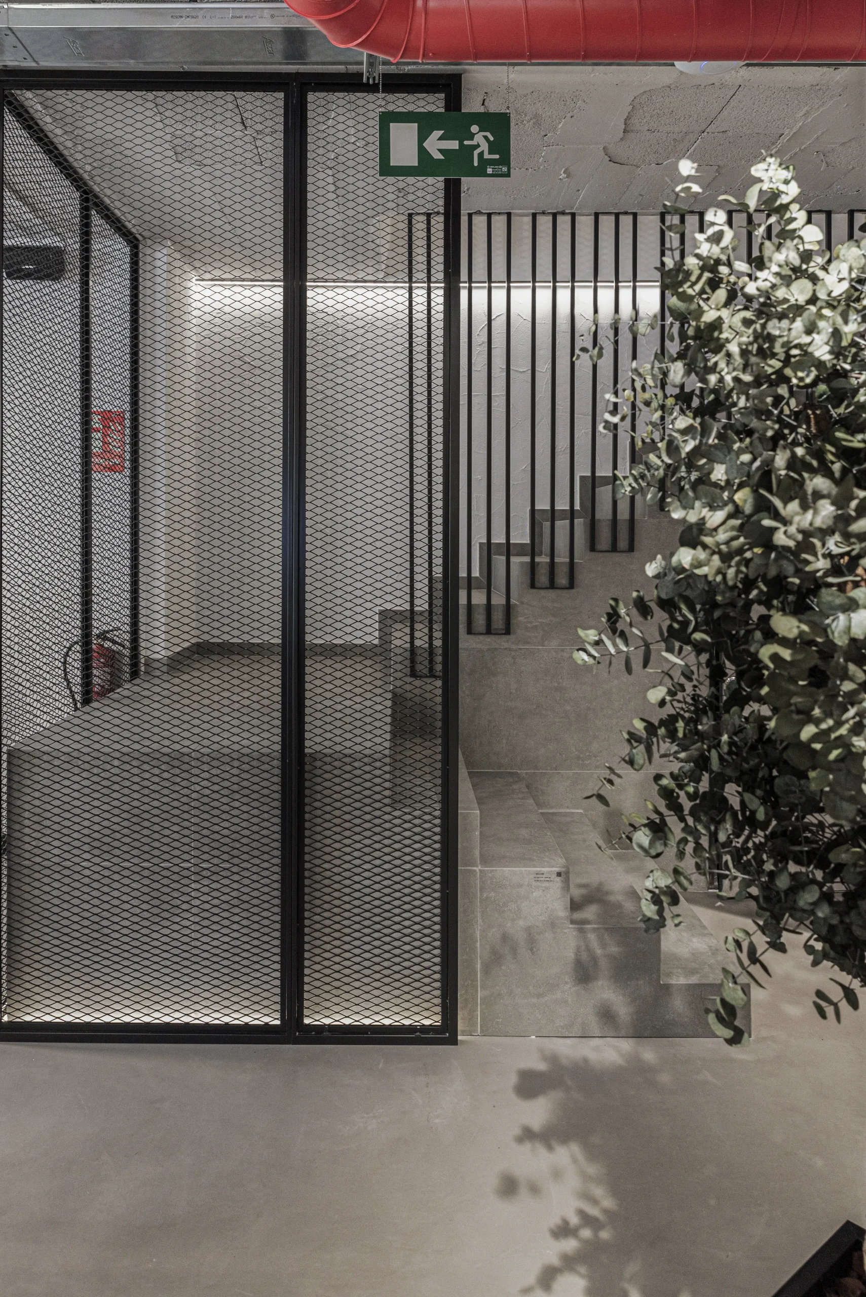 Puerta corredera de malla metálica y escalera de hormigón con celosía de barrotes negros en la tienda SALONI de Alicante