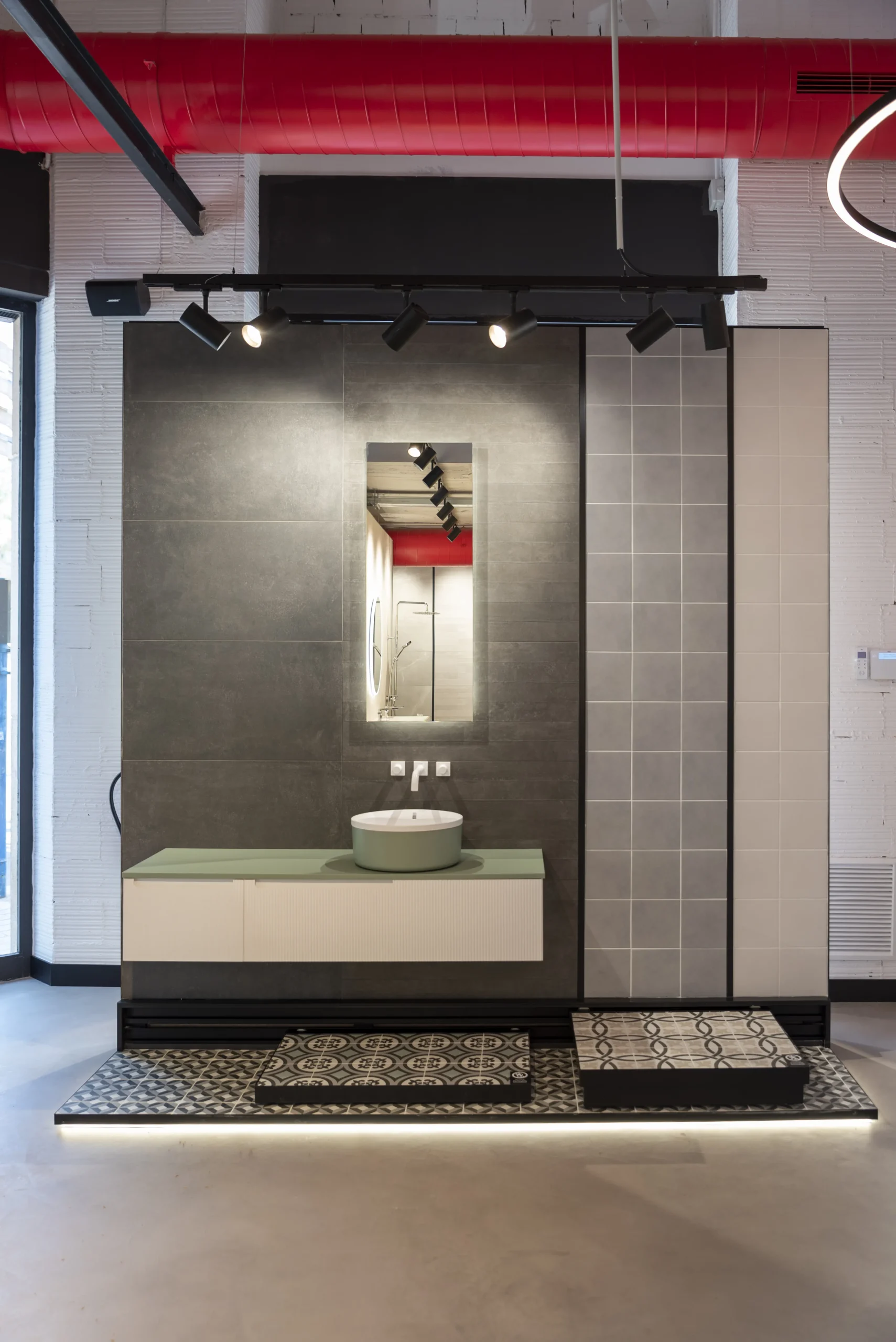 Mueble de baño con lavabo sobre encimera verde, espejo retroiluminado y revestimiento cerámico gris en la tienda SALONI de Alicante