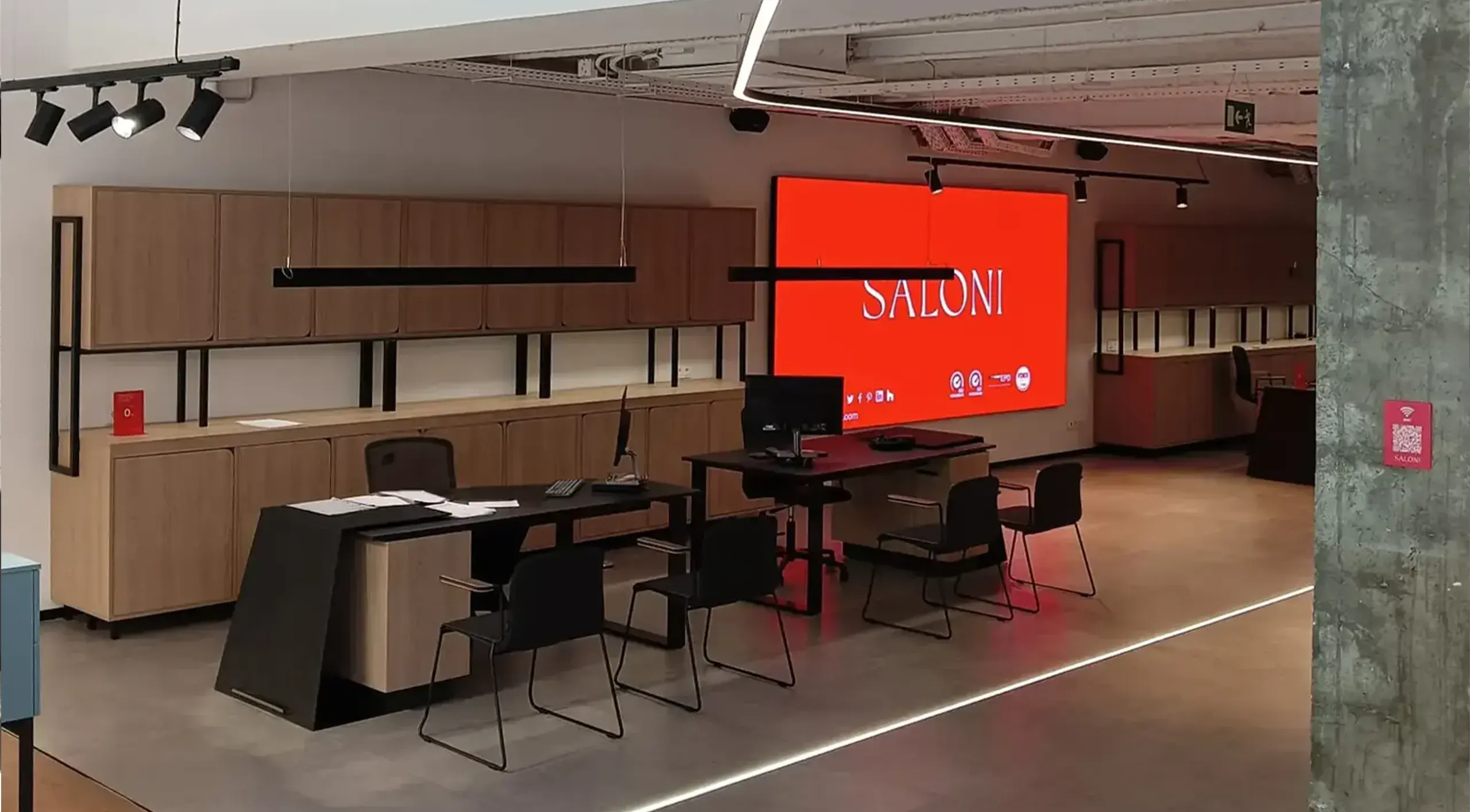 Puesto de venta de SALONI Madrid con mueble de madera, mesas de atención al cliente y una gran pantalla LED con el logotipo de la marca