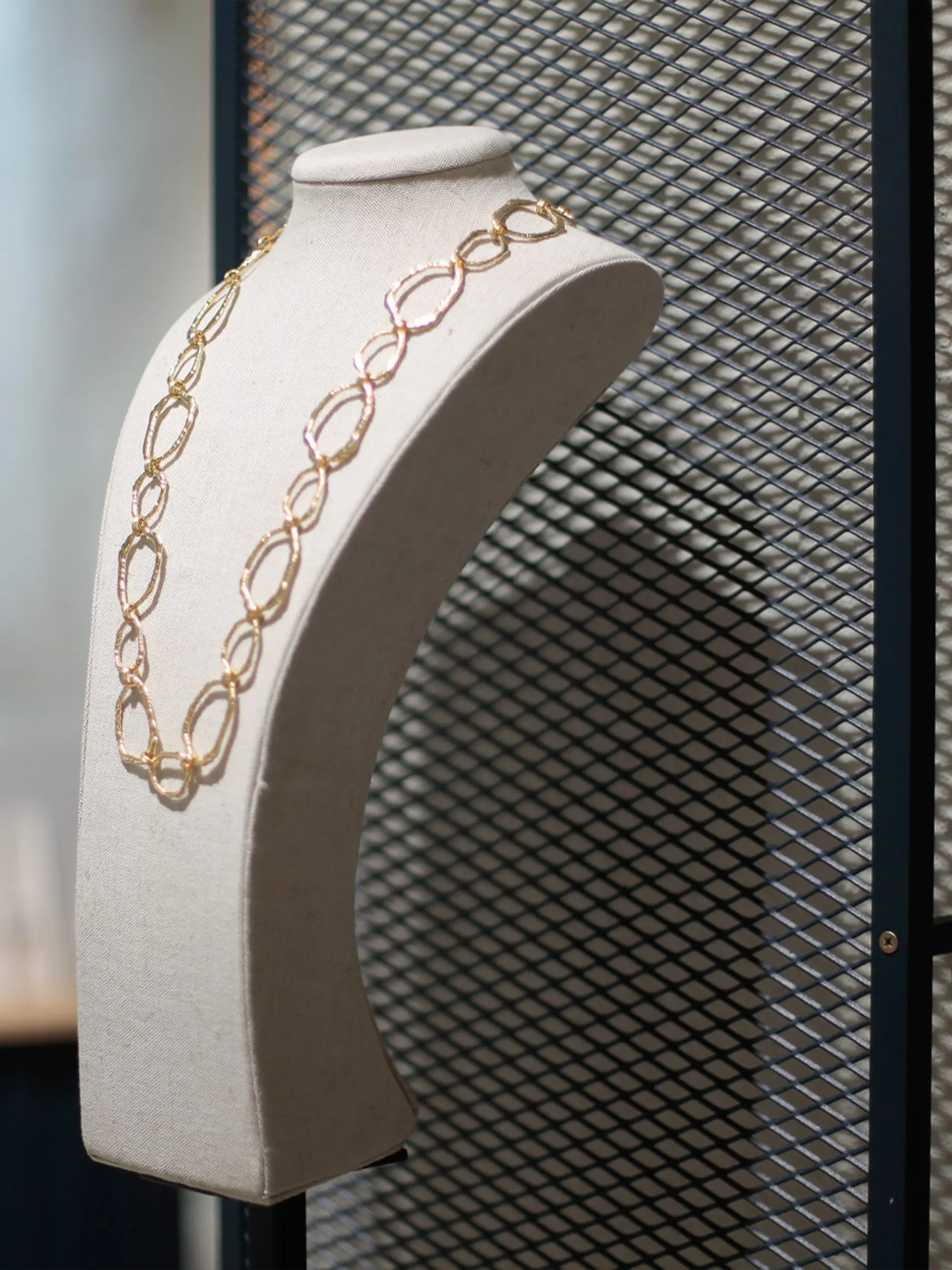 Collar de cadena dorada expuesto en maniquí sobre fondo de malla metálica