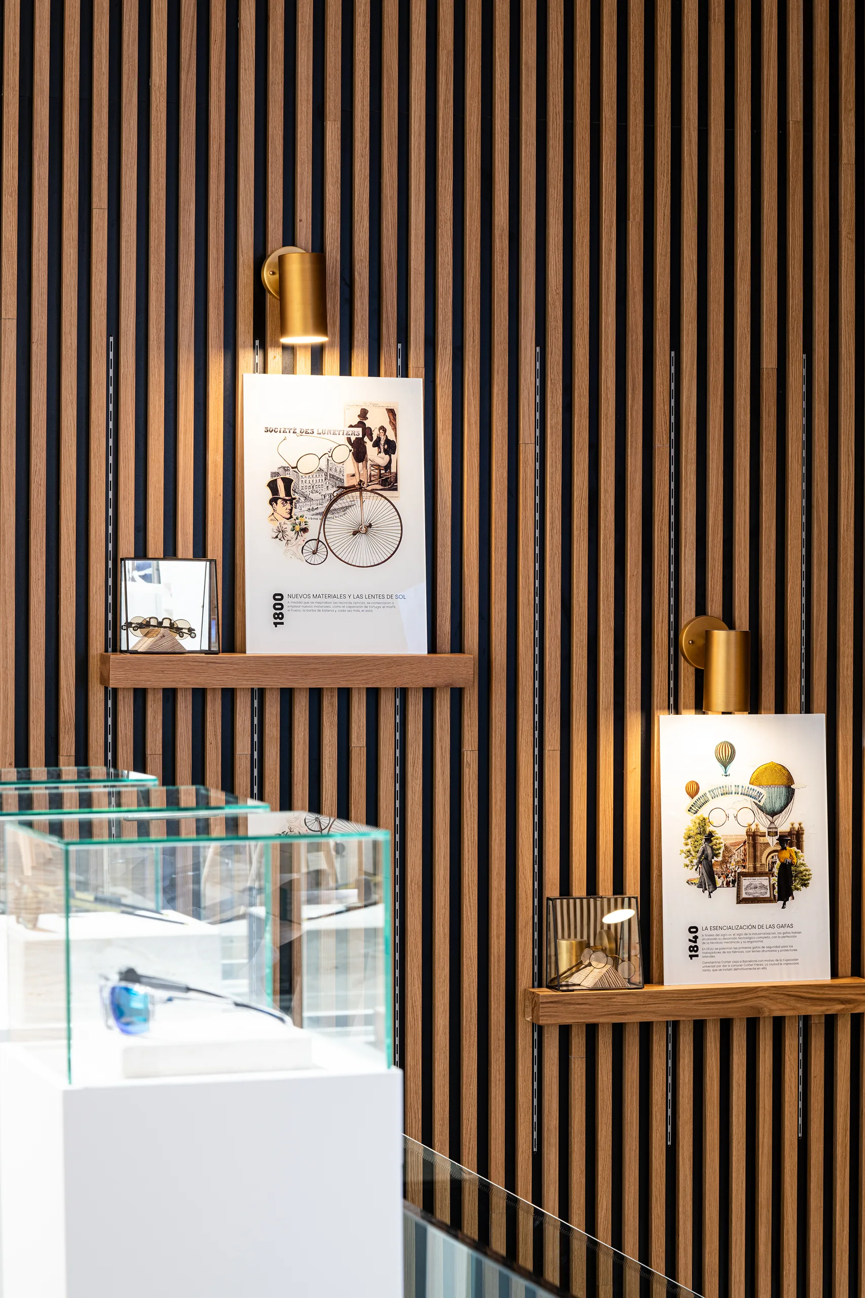 Pared de lamas de madera con la línea temporal de la historia de la óptica y vitrinas de gafas antiguas en el flagship de Cottet
