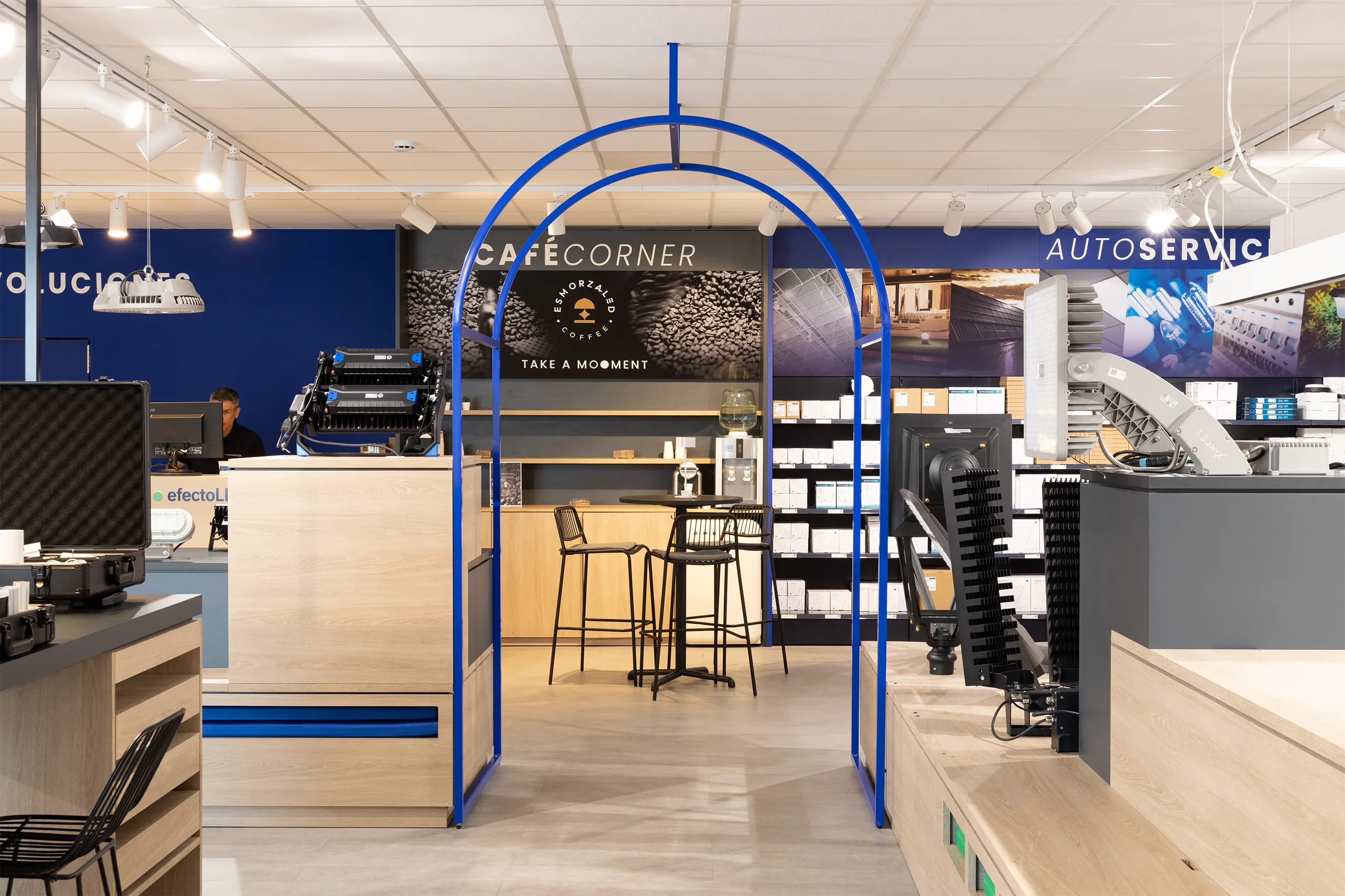 Arco de estructura tubular azul que da acceso a Café Corner, la cafetería interior de efectoLED en Catarroja, con el rótulo «Take a mooment»