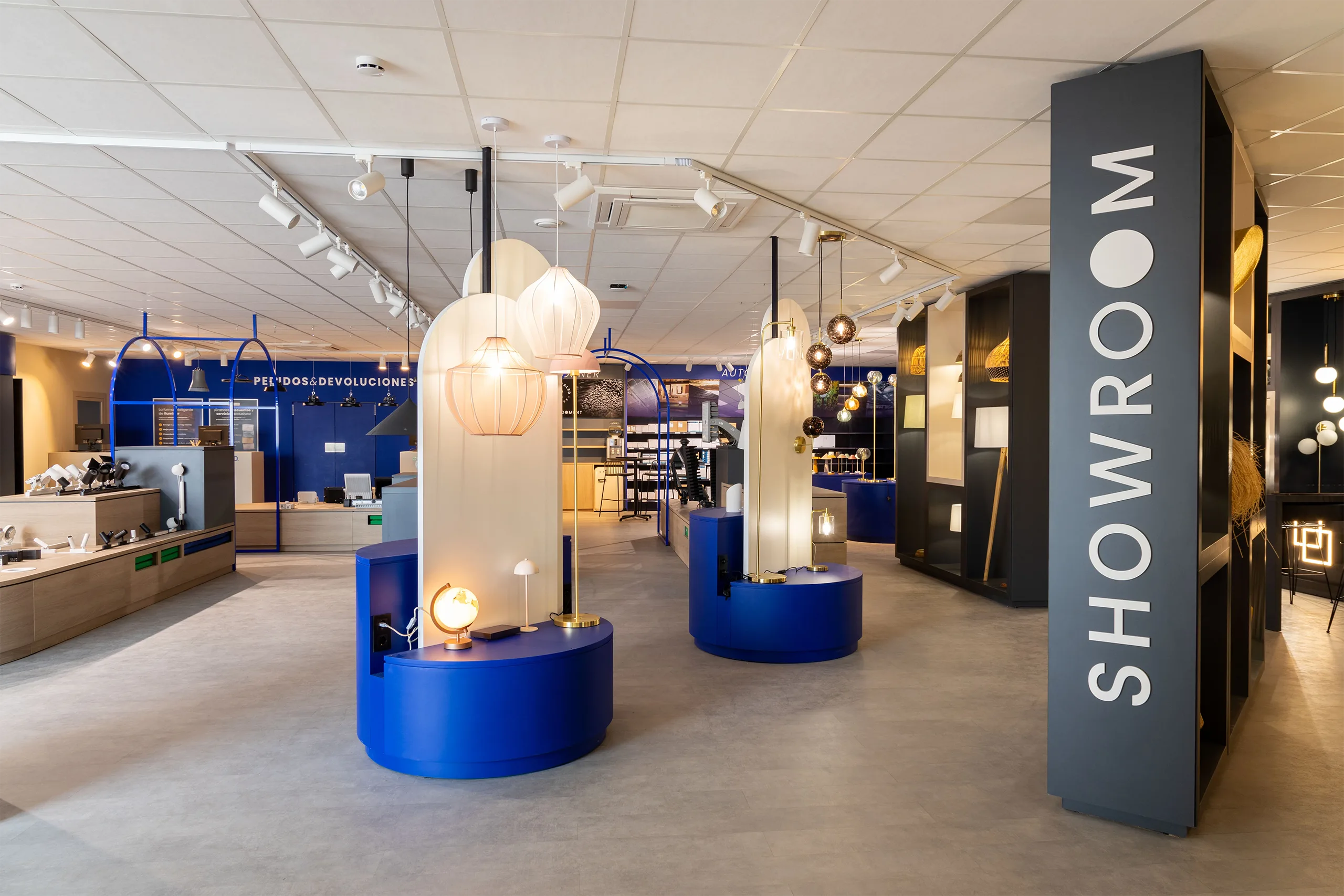 Zona Showroom de efectoLED en Catarroja con mostradores circulares en azul corporativo, lámparas colgantes en tonos cálidos y el rótulo vertical «Showroom» al fondo