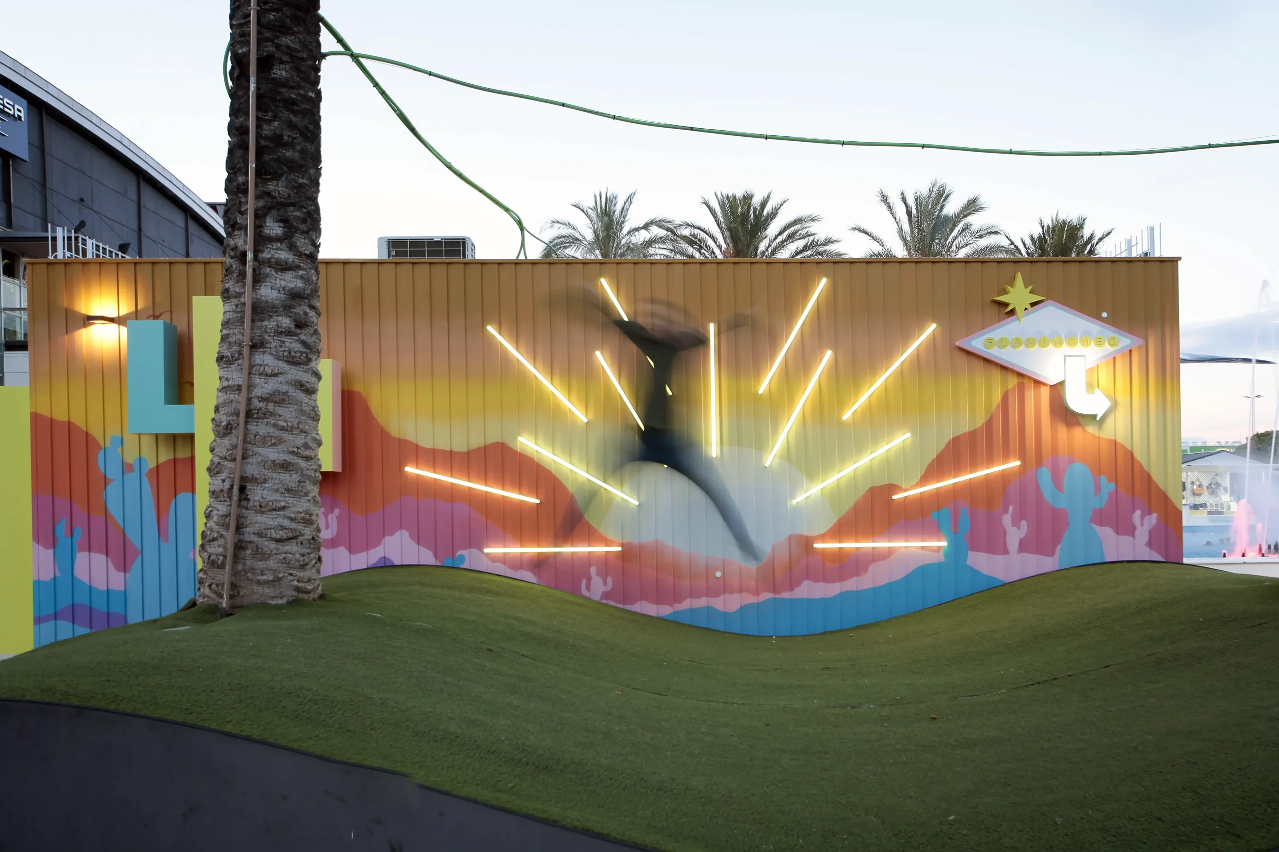 Mural photocall de desierto al atardecer con rayos LED, cartel estilo Las Vegas y persona saltando