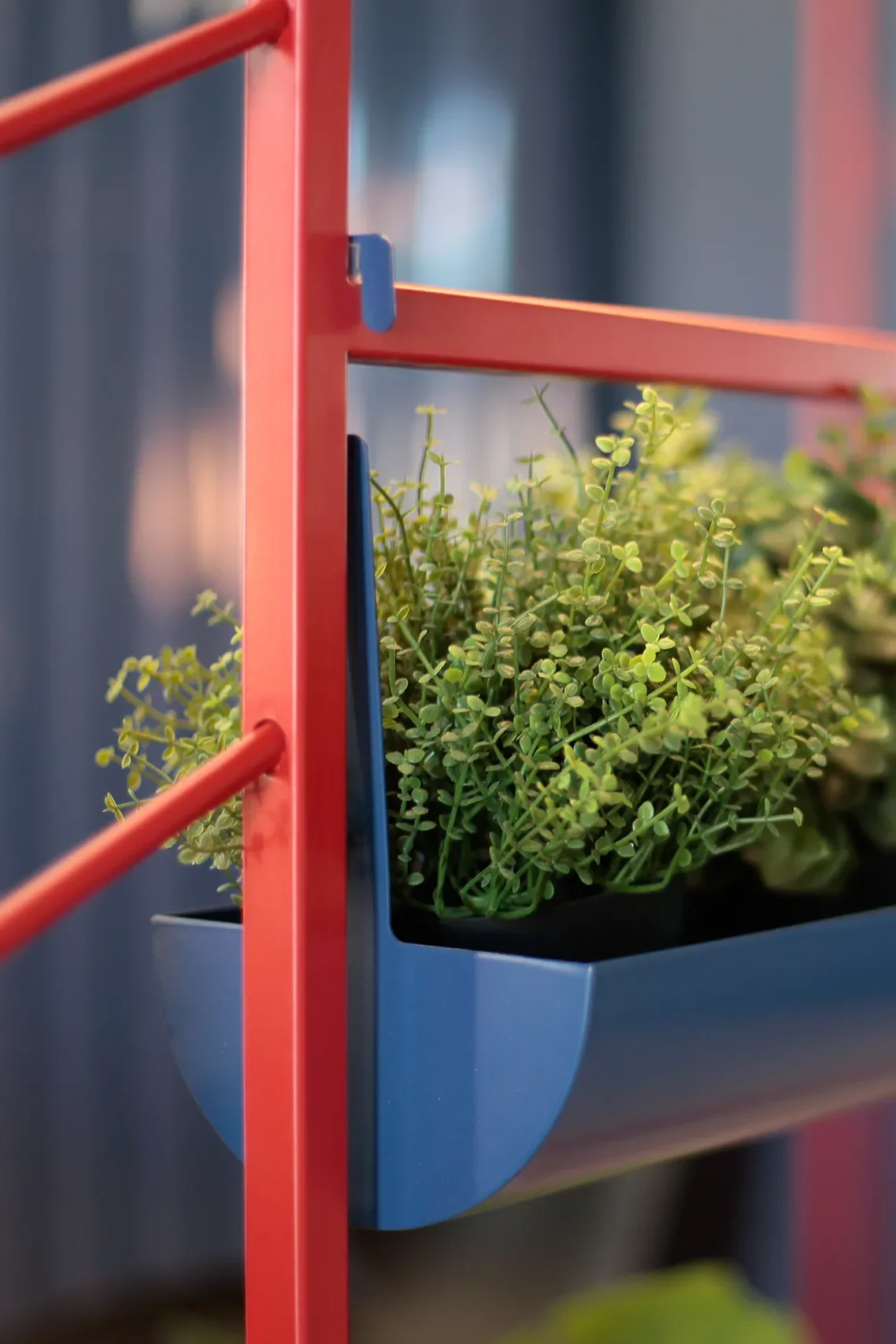 Detalle de la jardinera en azul petróleo integrada en la estructura de chapa roja de KeyGo Rent, oficina de alquiler de coches en Alicante