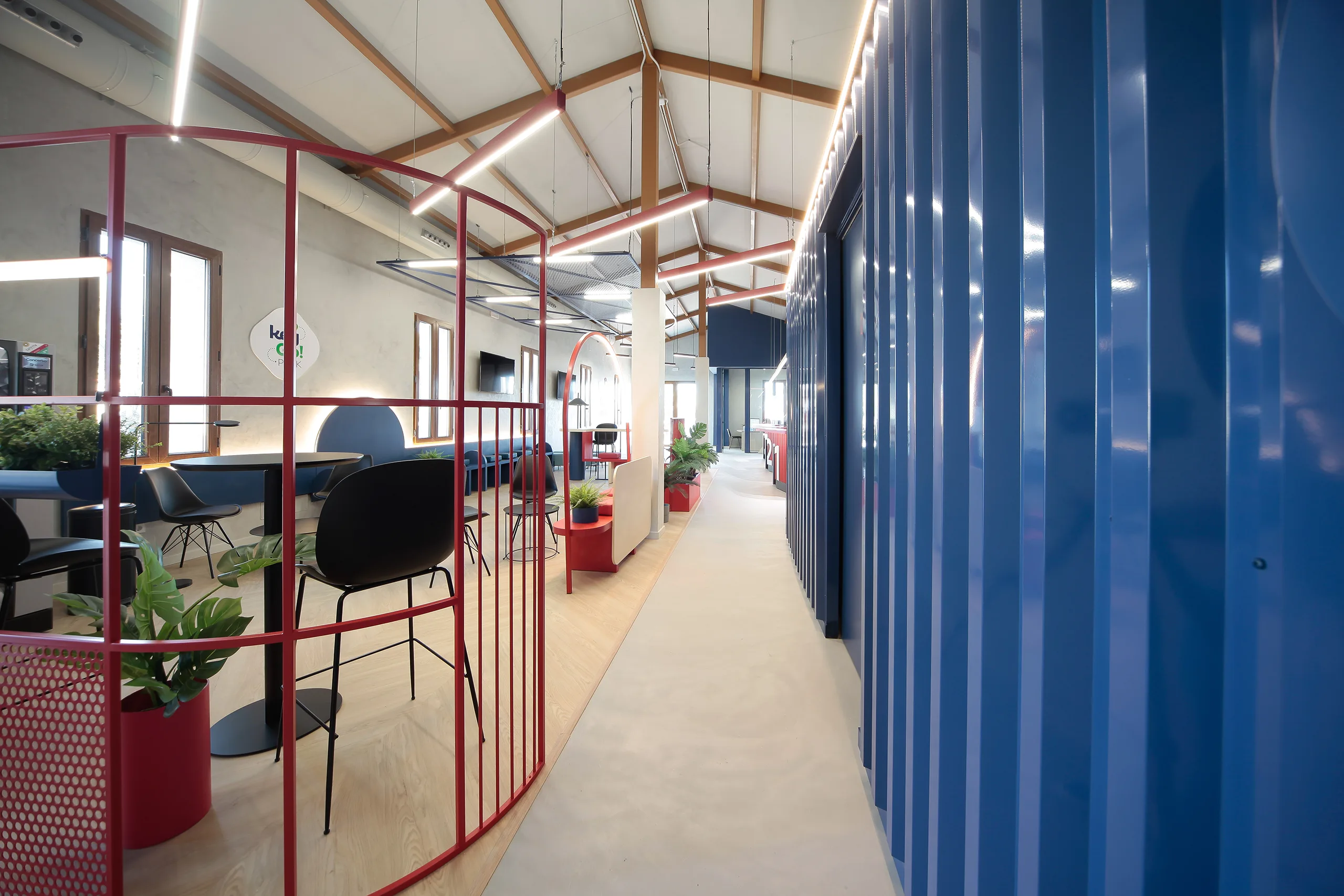 Pasillo de KeyGo Rent con celosía roja en primer plano, zona de espera con mobiliario azul y panel acanalado en azul petróleo, oficina de alquiler de coches en Alicante