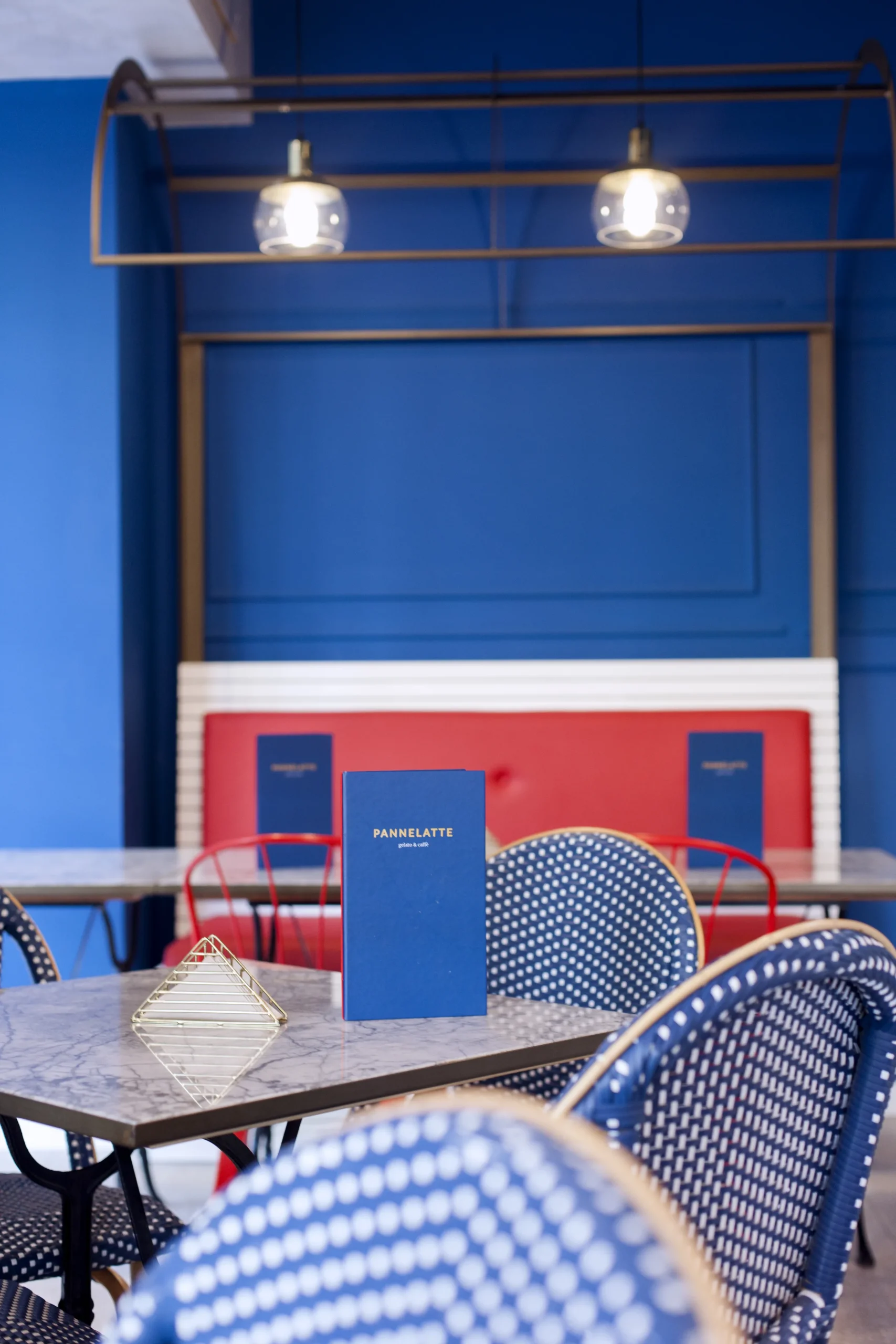 Zona de mesas de Pannelatte con banqueta roja, sillas bistró azules y mesas altas de mármol, heladería italiana en Mallorca diseñada por huuun