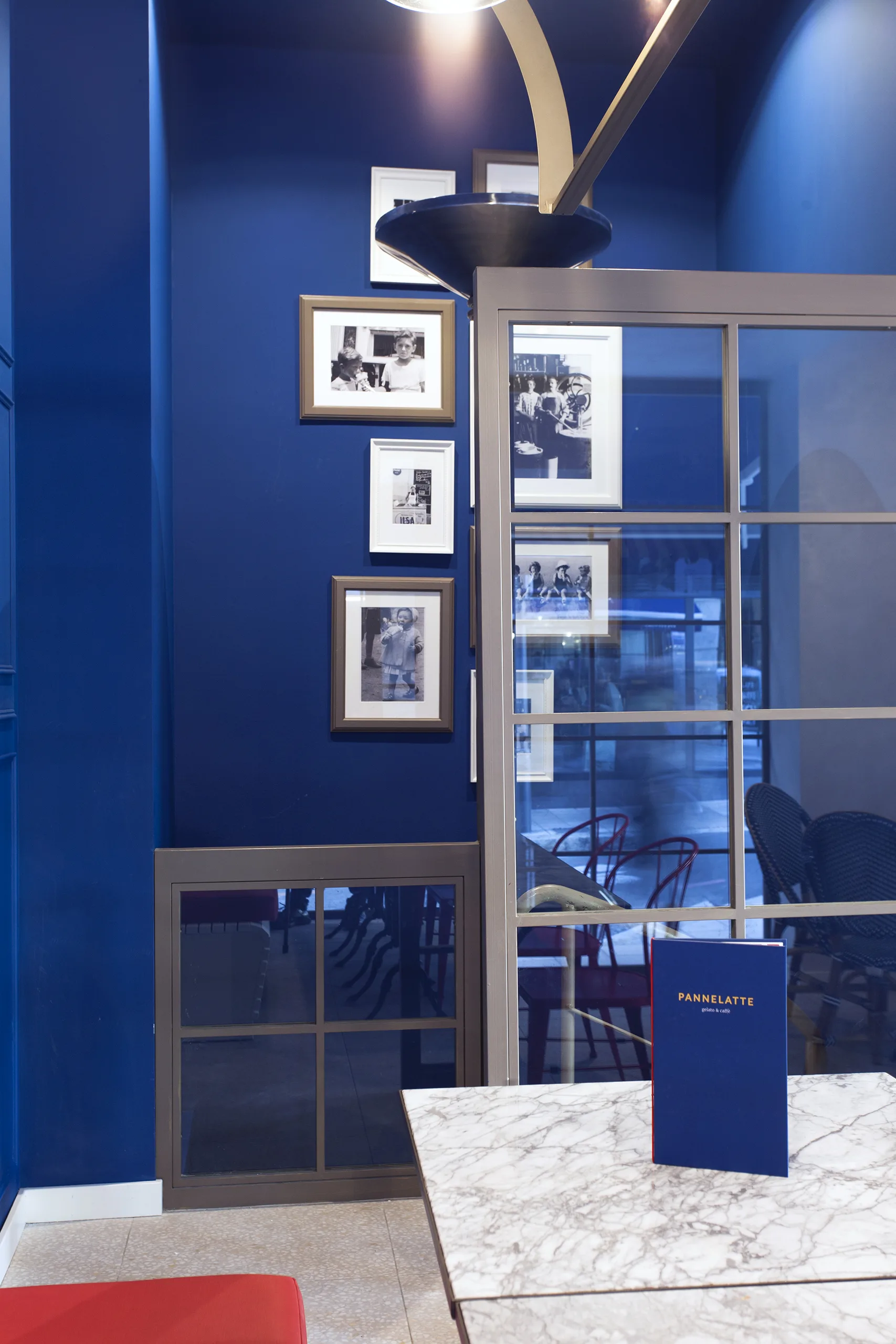 Fotografías familiares en blanco y negro sobre pared azul marino, junto a la carta de Pannelatte en una mesa de mármol, heladería italiana en Mallorca