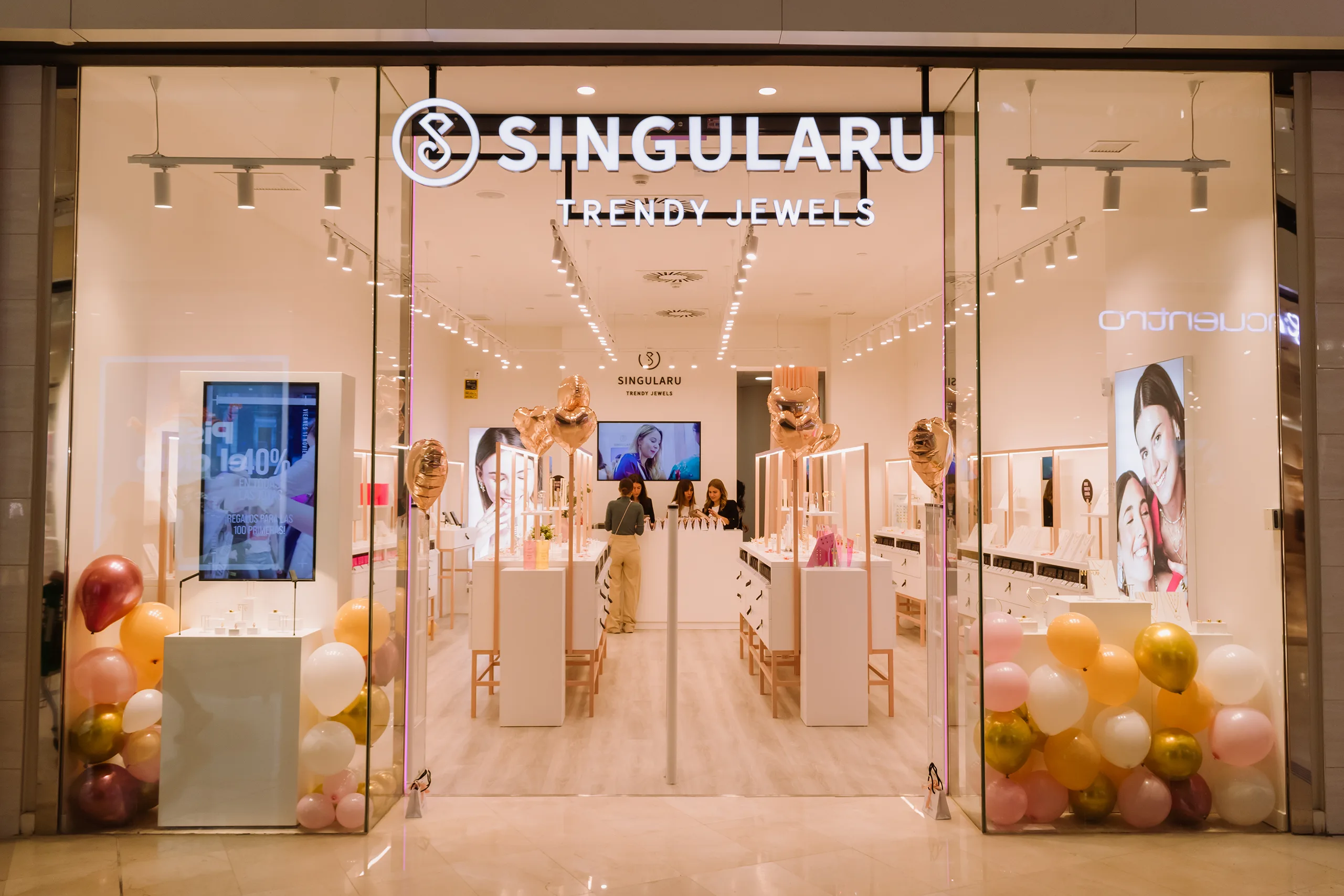 Entrada de Singularu en un centro comercial decorada con globos y corazones metalizados, con mostradores blancos al fondo