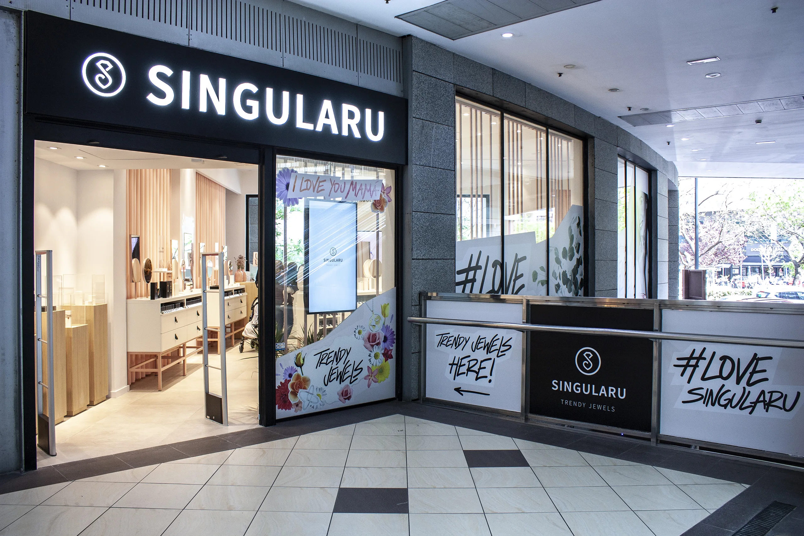 Fachada de Singularu en un centro comercial con vinilos de flores, «I love you mamá» y cartel #LOVE Singularu