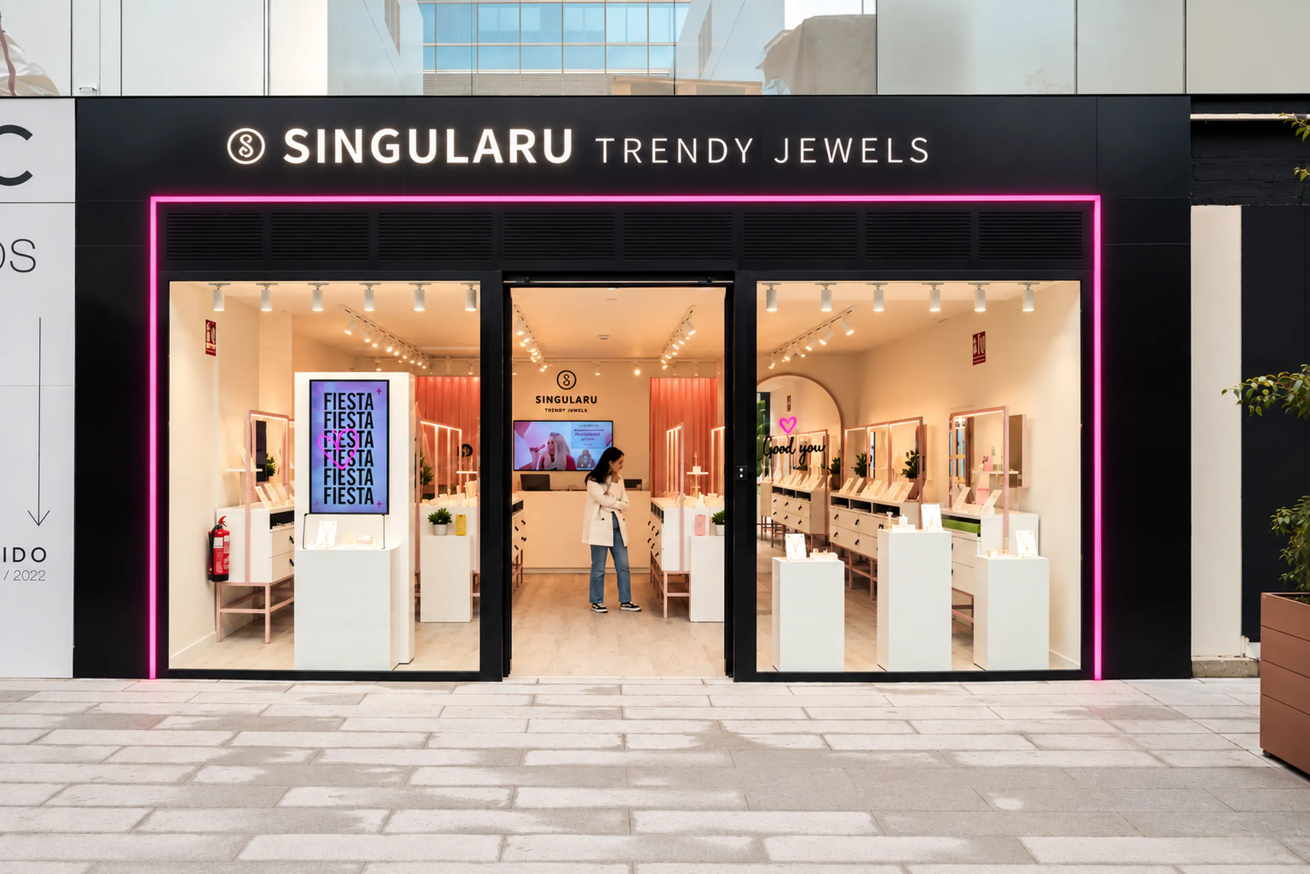 Fachada negra de Singularu Trendy Jewels con marco de neón rosa y escaparates con mostradores blancos