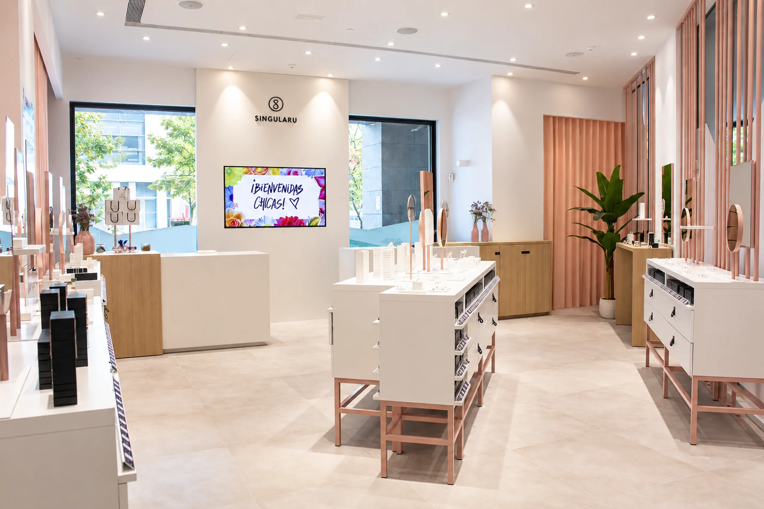 Interior de la tienda Singularu con mostradores blancos, cortina rosa, planta y pantalla de bienvenida