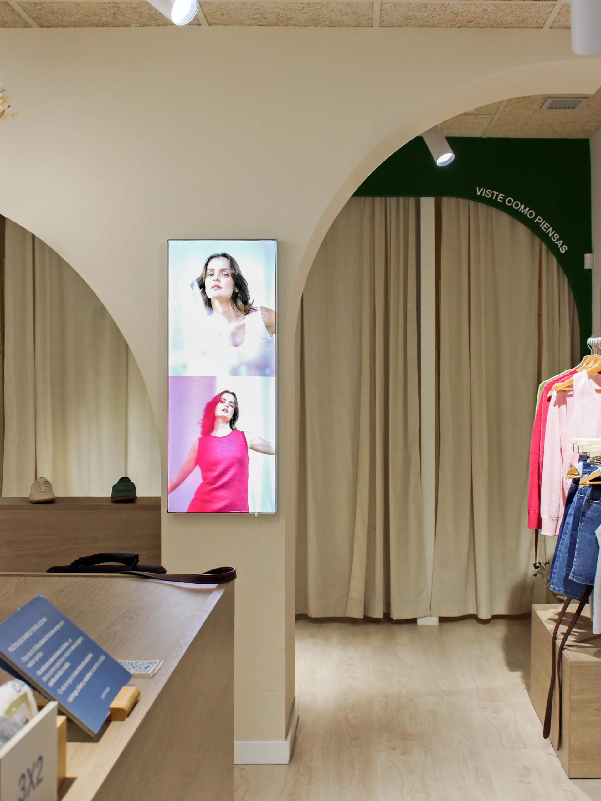 Arcos en tonos tierra con cortinas de lino en los probadores, pantalla vertical y arco verde con el mensaje «Viste como piensas»
