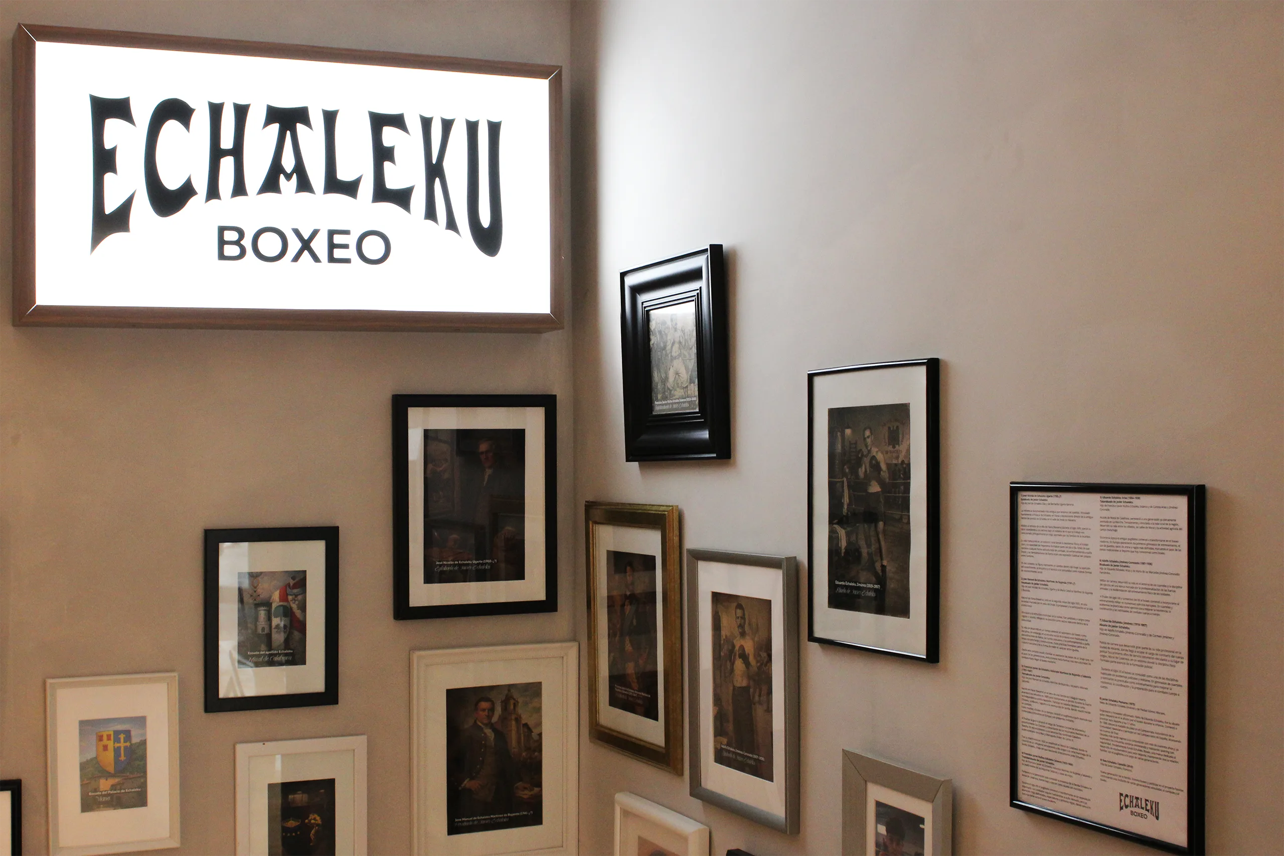 Caja de luz «Echaleku Boxeo» junto a una pared de fotografías enmarcadas de historia familiar