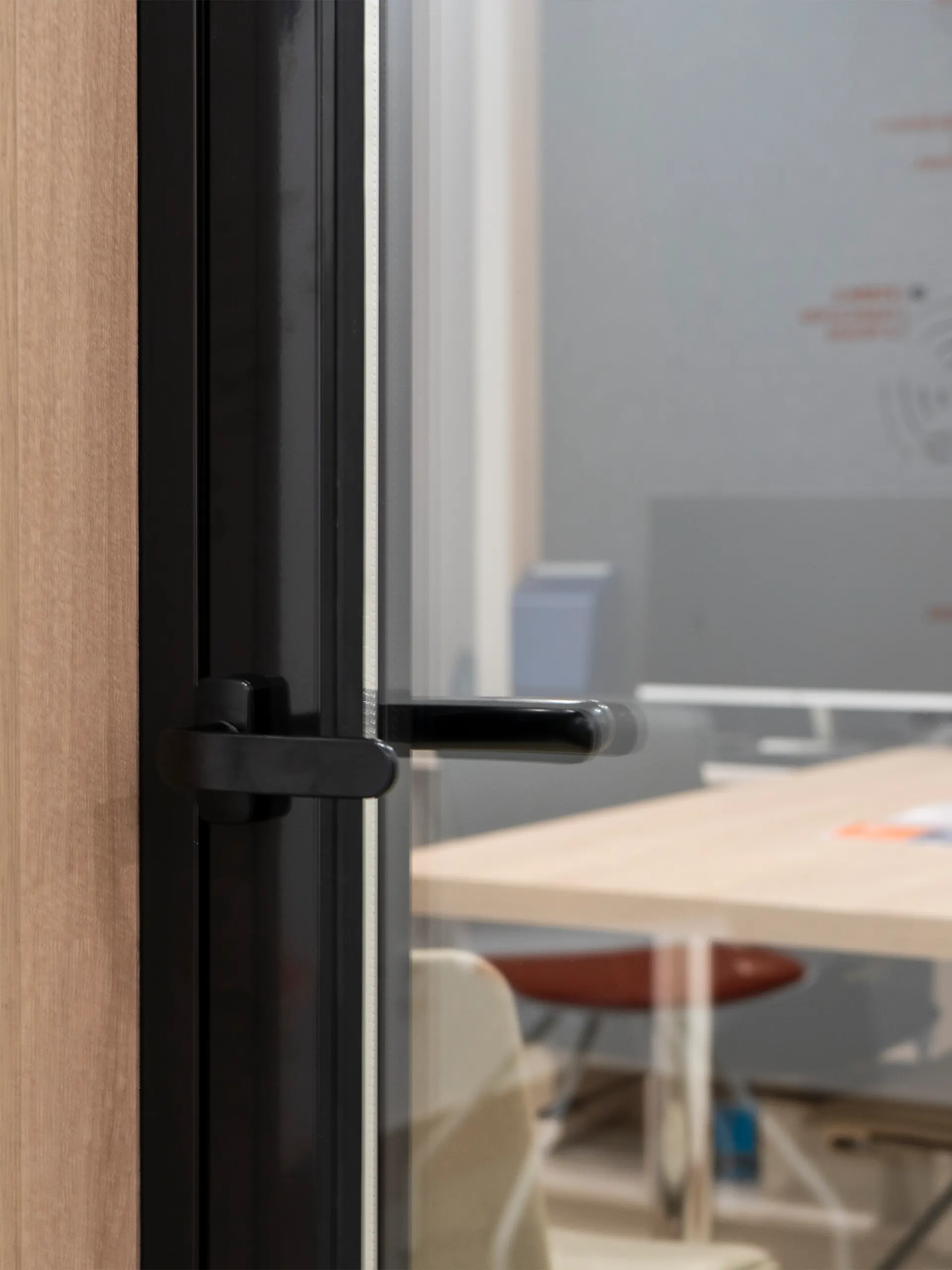 Detalle de la manilla negra de una puerta de vidrio con perfil negro junto a un marco de madera en GrandAudition