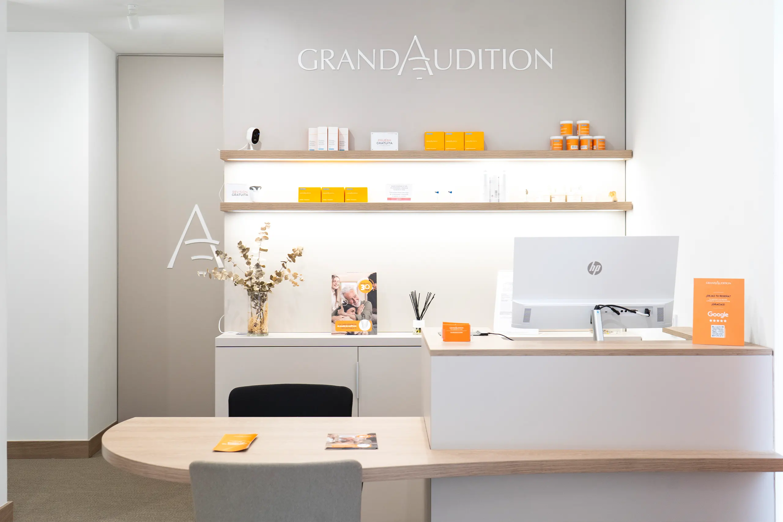 Mostrador de recepción de GrandAudition con encimera curva de madera, estanterías iluminadas y logotipo sobre pared gris