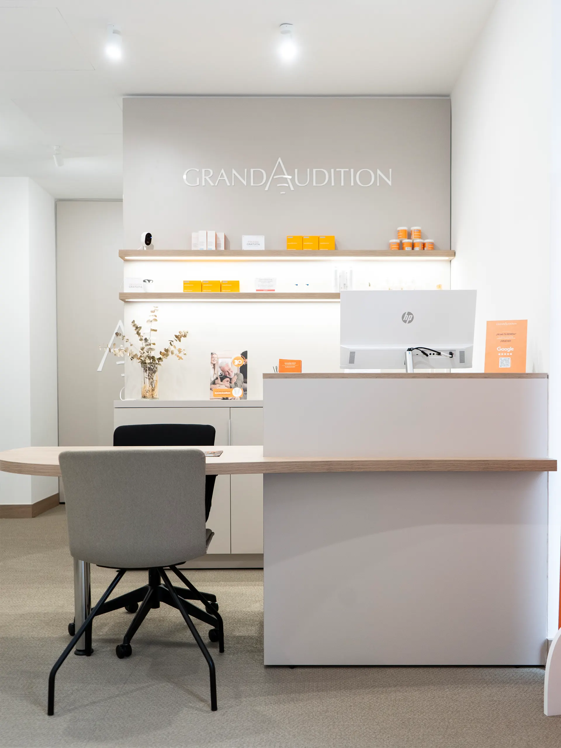 Mostrador de recepción de GrandAudition con encimera de madera, estanterías iluminadas y logotipo de la marca sobre pared gris
