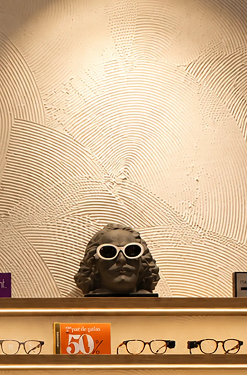 Detalle del relieve de mortero de cal beige con un busto clásico que lleva gafas de sol blancas en la óptica Quevedos